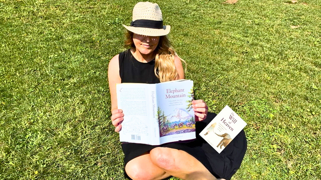 Debbie Ethell, elephant conservation scientist and author laying in the grass on a summer day reading one of her books.