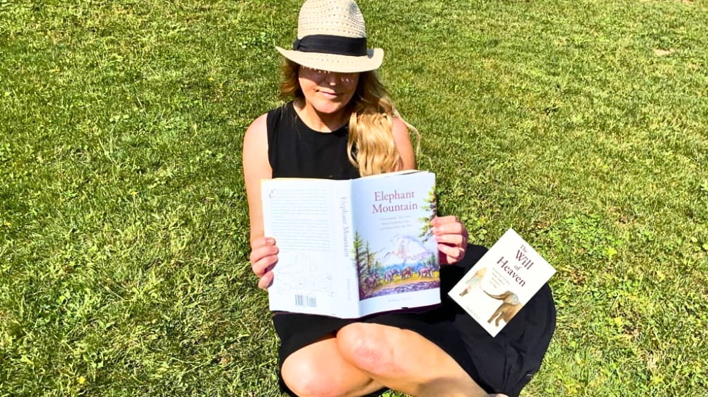 Debbie Ethell, author of The Will of Heaven memoir series, relaxing in the grass while reading one of her books about elephants.