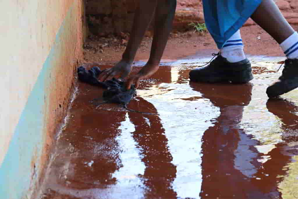 Student mopping a wet classroom floor after heavy rain.