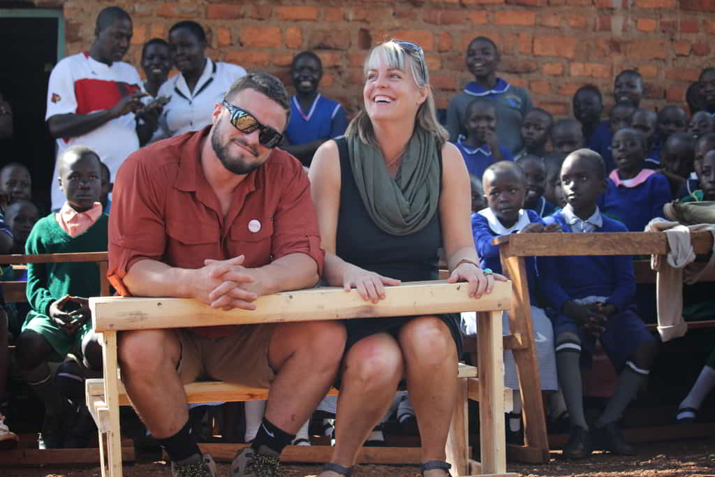 Debbie Ethell with a KOTA team member sitting at newly built school desk in Kakamega surrounded by students.