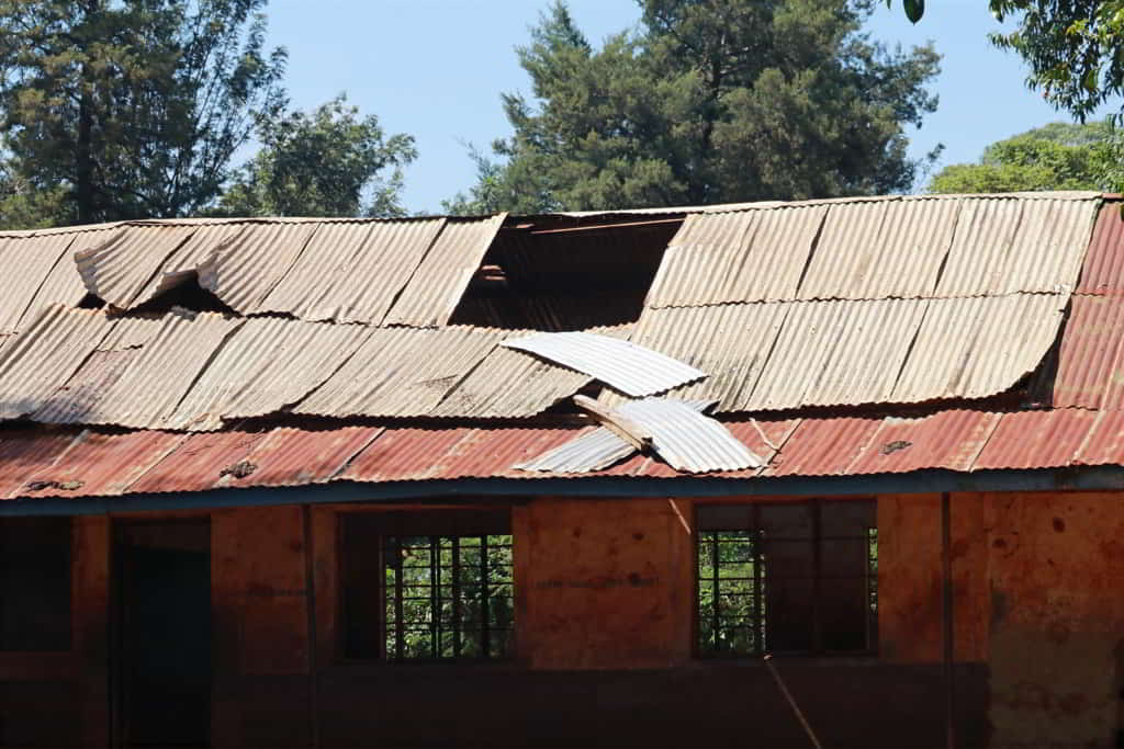 Damaged tin roof of a school with a large hole allowing rainwater into the classroom.