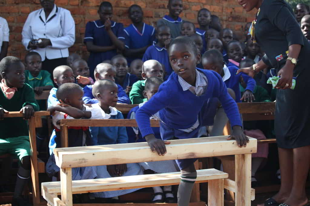 Young Kenyan child sitting at a newly built school desk while other students sit behind her.