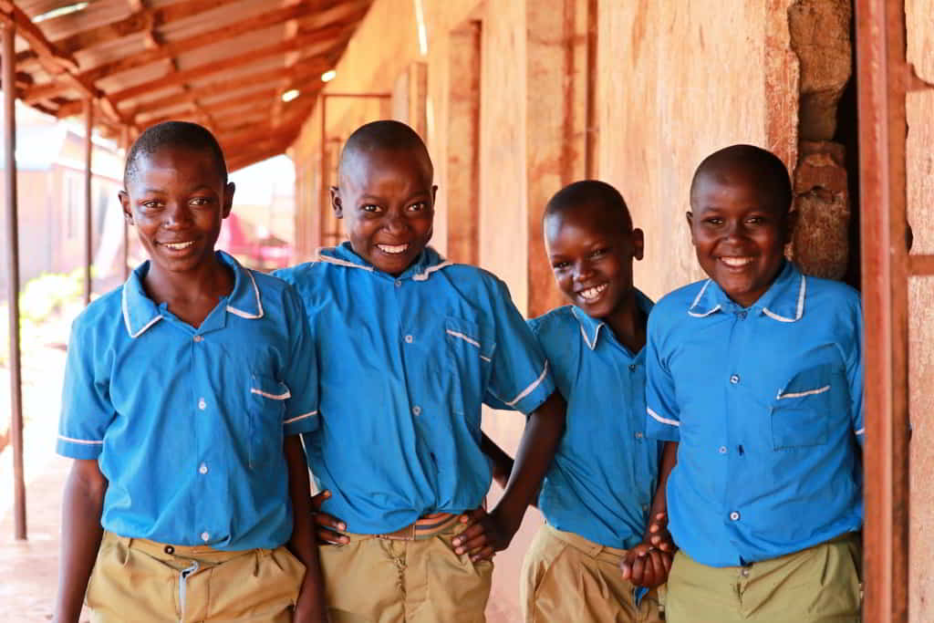 Four Kenyan schoolboys in bright blue uniforms smiling at the camera.