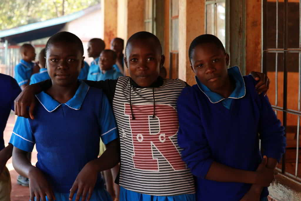 Three Kenyan schoolgirls in uniform looking directly at the camera wtih calm, satisfied expressions.