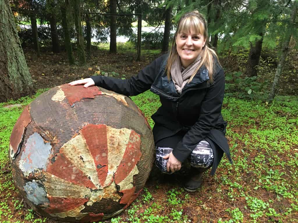 Author Debbie Ethell posing next to a rusted circus elephant ball in the woods on Elephant Mountain.